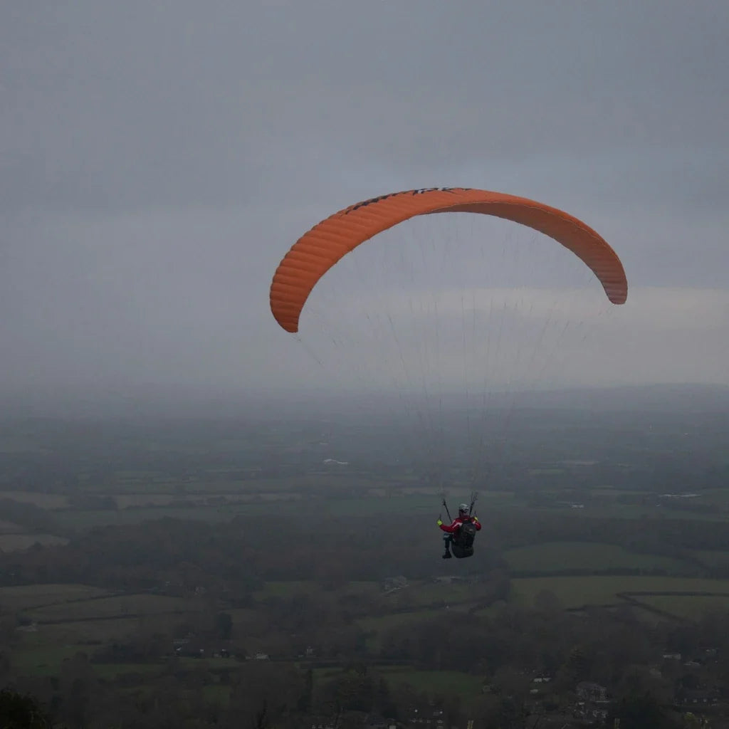 Personne en parapente au-dessus d'un paysage, illustrant une activité à sensations fortes en pleine nature.