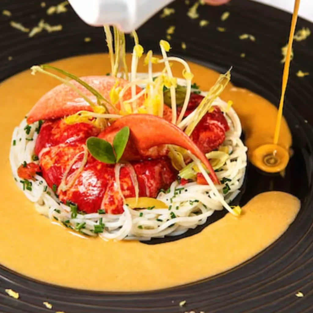 Assiette de haute gastronomie avec homard, pâtes fines et sauce servie à table, illustrant l'expérience d'un dîner gastronomique étoilé.